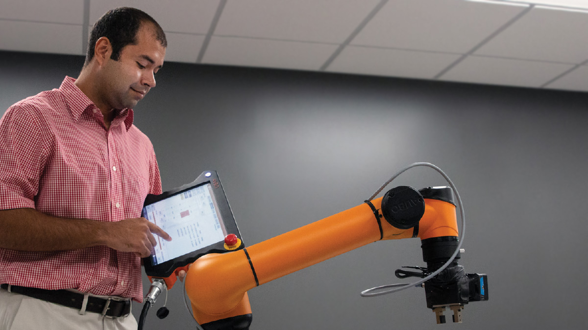 Jose Bonilla uses a touch screen to control a bright orange robotic arm
