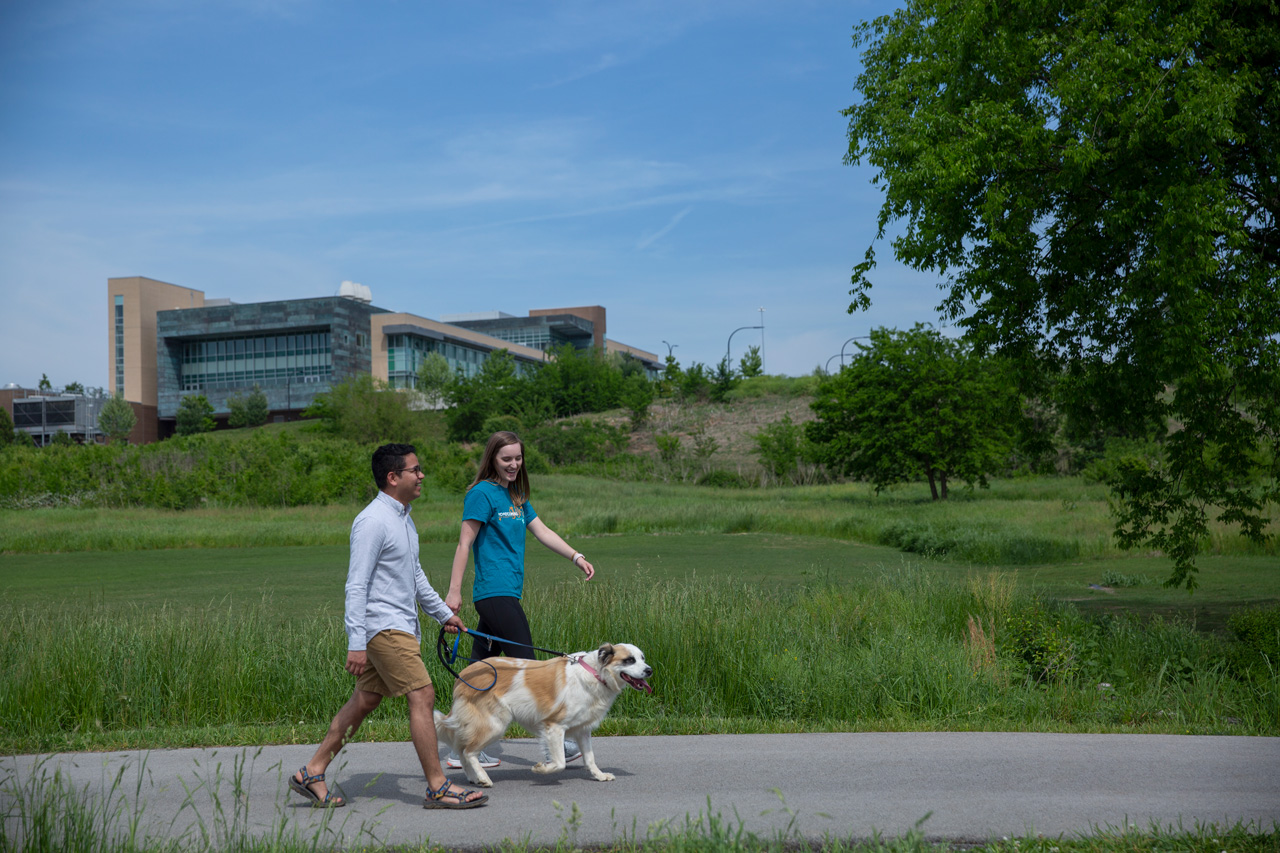Two people walk their dog on the Cherokee Farm grounds on the paved trail