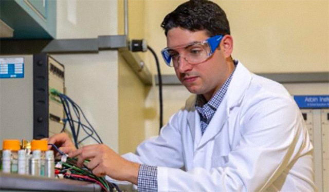 A man in safety googles connects wiring to a tech experiement